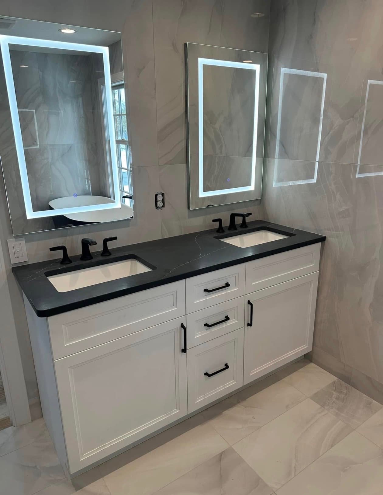Double vanity with a dark stone top and lighted mirrors in a finished bath remodel